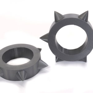 May include: Two grey, plastic rings with pointed spikes around the outside. The rings are approximately 5 cm in diameter.