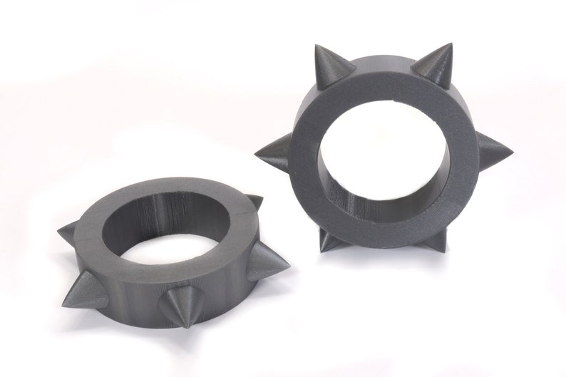 May include: Two grey, plastic rings with pointed spikes around the outside. The rings are approximately 5 cm in diameter.