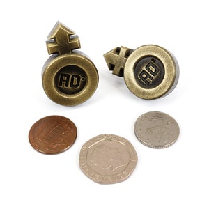 May include: Two gold-colored metal tokens with the symbol for male and female on top and the letters "AD" with a superscript 2 in the center.  There are three coins below the tokens.