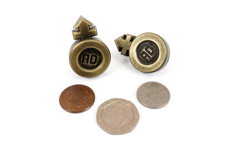 May include: Two gold-colored metal tokens with the symbol for male and female on top and the letters "AD" with a superscript 2 in the center.  There are three coins below the tokens.