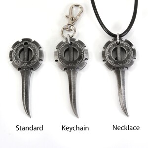 May include: Three silver-toned metal pendants with a circular design and a pointed blade. The pendants are shown in three different styles: standard, keychain, and necklace.