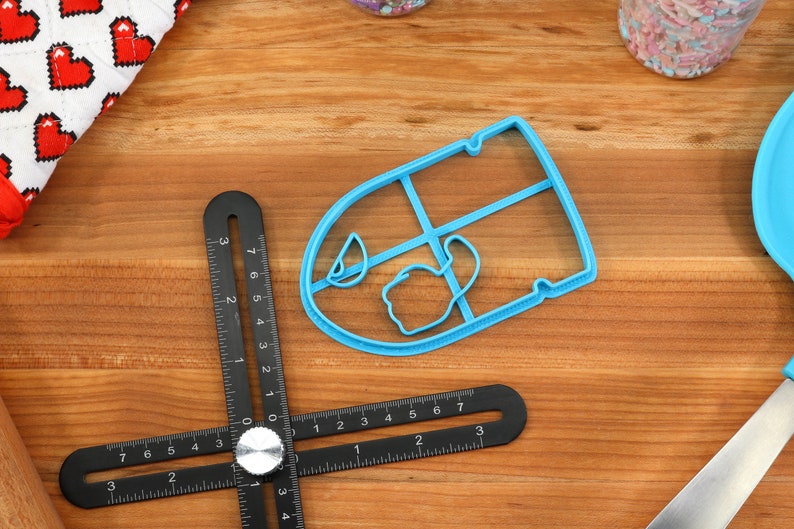 May include: A blue plastic cookie cutter shaped like a teacup with a handle. The cutter is on a wooden surface with a black ruler.