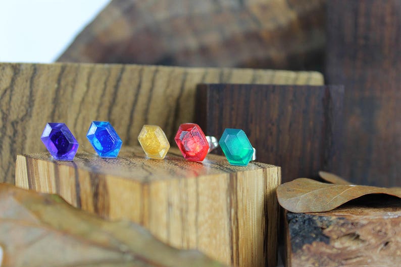 May include: Five small, faceted, gemstone-like objects in various colors, including purple, blue, gold, red, and green, are arranged on a wooden surface.