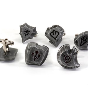 May include: Six silver cufflinks with different shield designs. Each shield has a unique symbol engraved on it.