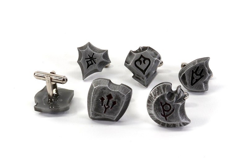 May include: Six silver cufflinks with different shield designs. Each shield has a unique symbol engraved on it.