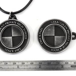 May include: A silver pendant necklace with a round charm featuring the words "Gekkoukan Private High School Since 1982" and a black and white checkered design.