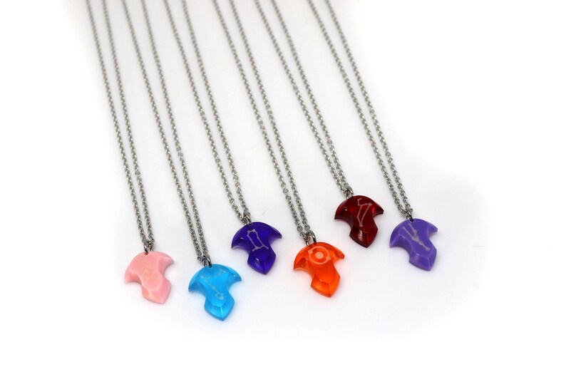 Puede incluir: Siete collares de plata con colgantes de diferentes colores. Los colgantes tienen forma de p&aacute;jaro con un dise&ntilde;o de constelaci&oacute;n. Los colores de los colgantes son rosa, azul, morado, rojo, naranja y dos tonos de morado.