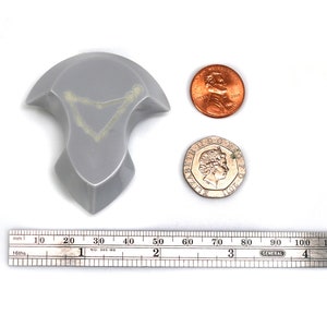 May include: A silver-colored, three-dimensional, abstract sculpture with a geometric shape. The sculpture is about 2 inches tall and 2 inches wide. It is sitting on a white surface next to a ruler and two coins.