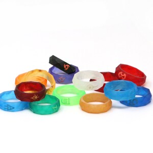 May include: A collection of 12 colorful silicone rings with different symbols. The rings are stacked and arranged in a semi-circle on a white background.