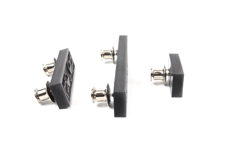 May include: Three gray plastic snap fasteners with silver metal posts. The fasteners are in different sizes and shapes.