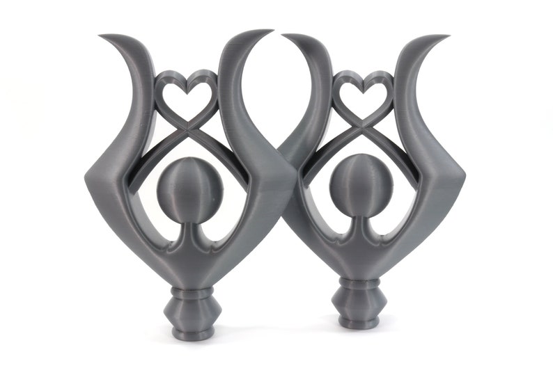 May include: Two gray, abstract sculptures with a heart and circle design. The sculptures are made of a smooth, matte material and have a modern, minimalist aesthetic.