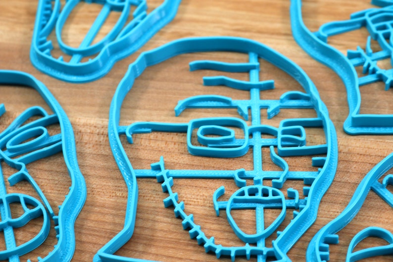 May include: A set of four blue plastic cookie cutters shaped like faces. The cutters are detailed with features like eyes, noses, and mouths.