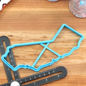 May include: A blue plastic cookie cutter shaped like the state of California. The cutter is on a wooden surface with a ruler.