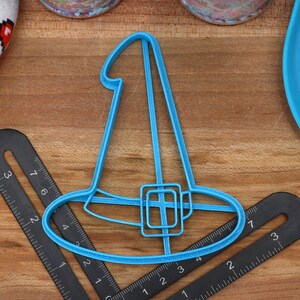 May include: A blue plastic witch hat cookie cutter. The cutter is about 4 inches wide and 3 inches tall.