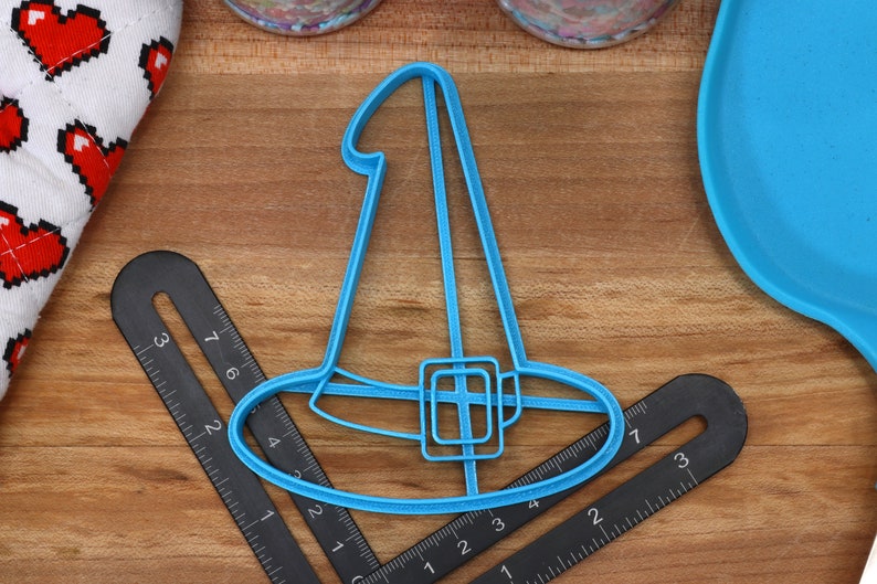 May include: A blue plastic witch hat cookie cutter. The cutter is about 4 inches wide and 3 inches tall.