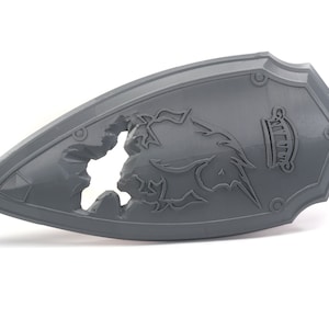 May include: A gray plastic shield with a damaged, textured surface. The shield has a raised design of a mythical creature with the word "GALLIVANT" inscribed on the surface.