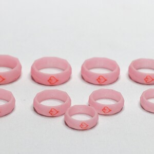 May include: A set of eight pink silicone rings with a red heart design. The rings are of varying sizes.