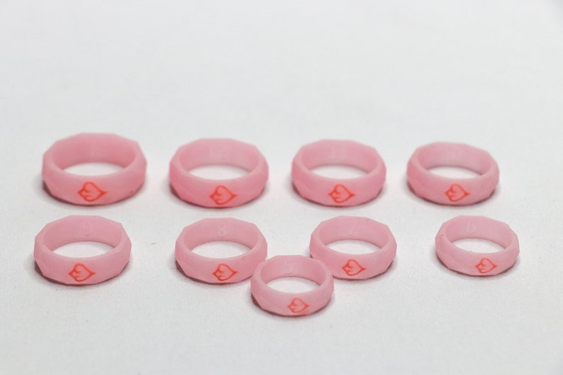 May include: A set of eight pink silicone rings with a red heart design. The rings are of varying sizes.