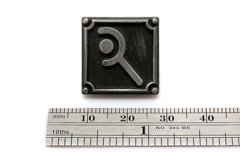 Peut inclure: Une &eacute;pingle en m&eacute;tal argent&eacute; avec un fond noir et un symbole stylis&eacute; d'un croissant de lune et d'un cercle. L'&eacute;pingle mesure environ 2,5 cm de large.