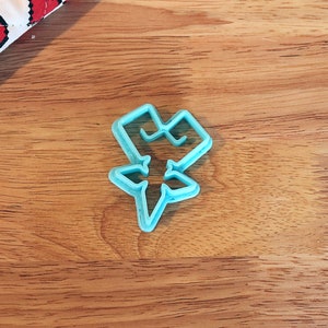 Pu&ograve; includere: Tagliapasta in plastica azzurra a forma di stella stilizzata. Il tagliapasta &egrave; su una superficie di legno, con una porzione di tessuto bianco e rosso a forma di cuore nell'angolo in alto a sinistra.