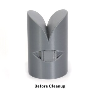 May include: A grey 3D printed object with a V-shaped design and a rectangular cutout in the centre. The object is sitting on a white surface. Before Cleanup.