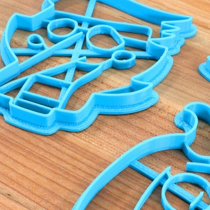 Peut inclure: Plusieurs emporte-pi&egrave;ces en plastique bleu clair de diff&eacute;rentes formes sont dispos&eacute;s sur une surface en bois. Les emporte-pi&egrave;ces semblent repr&eacute;senter un voilier, une paire de ciseaux et d'autres motifs abstraits. L'image est bien &eacute;clair&eacute;e, mettant en valeur les d&eacute;tails des emporte-pi&egrave;ces.