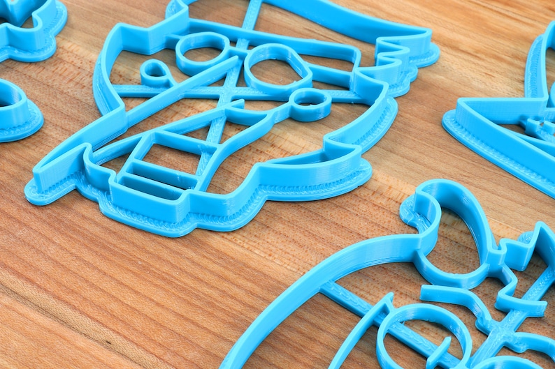 Peut inclure: Plusieurs emporte-pi&egrave;ces en plastique bleu clair de diff&eacute;rentes formes sont dispos&eacute;s sur une surface en bois. Les emporte-pi&egrave;ces semblent repr&eacute;senter un voilier, une paire de ciseaux et d'autres motifs abstraits. L'image est bien &eacute;clair&eacute;e, mettant en valeur les d&eacute;tails des emporte-pi&egrave;ces.