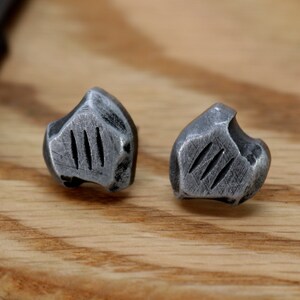 May include: A pair of silver-toned metal earrings with a textured, irregular shape and three vertical lines on each earring.