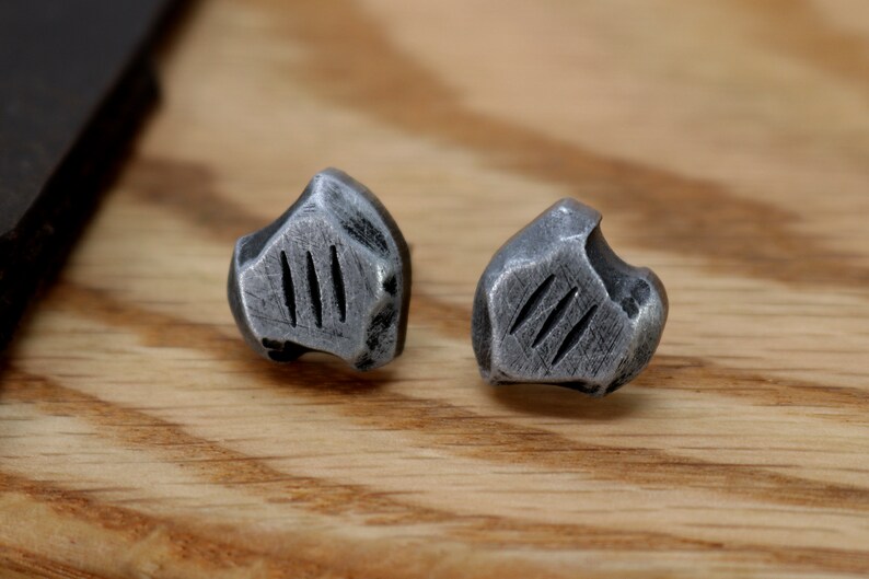 May include: A pair of silver-toned metal earrings with a textured, irregular shape and three vertical lines on each earring.