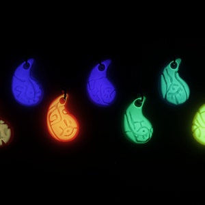May include: Seven glow-in-the-dark pendants in different colours, including white, blue, green, orange, and yellow. Each pendant is shaped like a teardrop and has a detailed design.