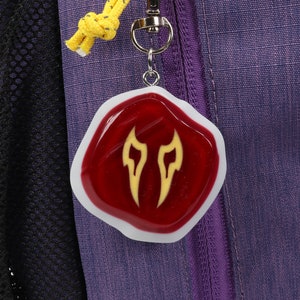 May include: A red resin keychain with a white border and a yellow flame design. The keychain is attached to a silver key ring.