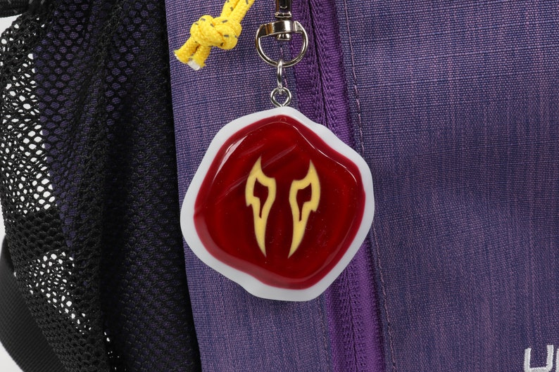 May include: A red resin keychain with a white border and a yellow flame design. The keychain is attached to a silver key ring.