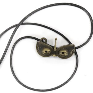 May include: A black cord necklace with a bronze pendant shaped like a robot face with large eyes and an antenna.