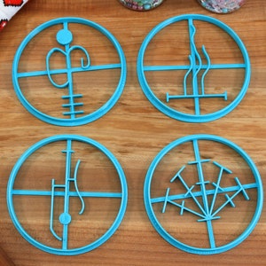 May include: Four blue plastic cookie cutters with different designs. The cutters are circular and have a raised design in the centre. The designs are abstract and geometric.