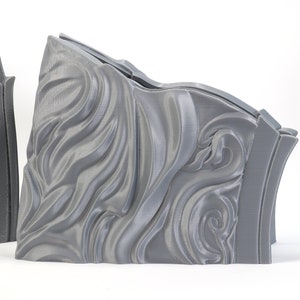 May include: Two gray 3D printed pieces with a decorative, swirling, wave-like pattern. The pieces are designed to fit together.