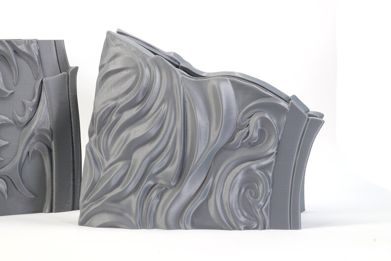 May include: Two gray 3D printed pieces with a decorative, swirling, wave-like pattern. The pieces are designed to fit together.