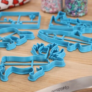 May include: A set of five blue plastic cookie cutters shaped like a moose, a fish, a bear, a Christmas tree, and a house.