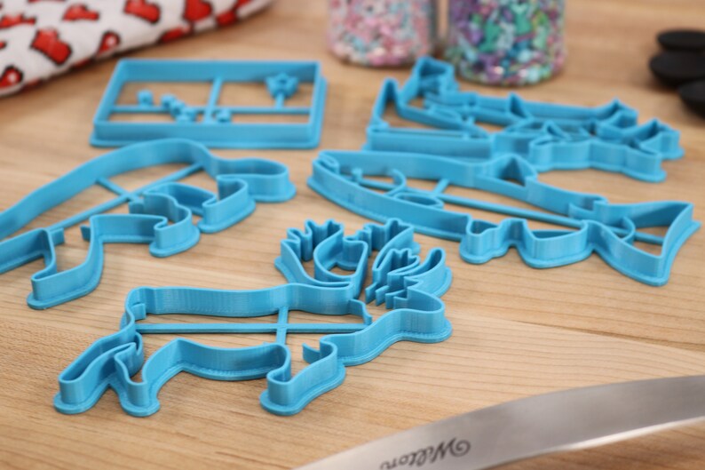 May include: A set of five blue plastic cookie cutters shaped like a moose, a fish, a bear, a Christmas tree, and a house.