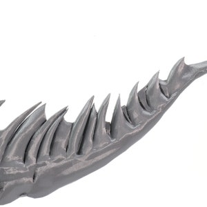 May include: A close-up of a gray, 3D printed, spiky tail with a sharp point.
