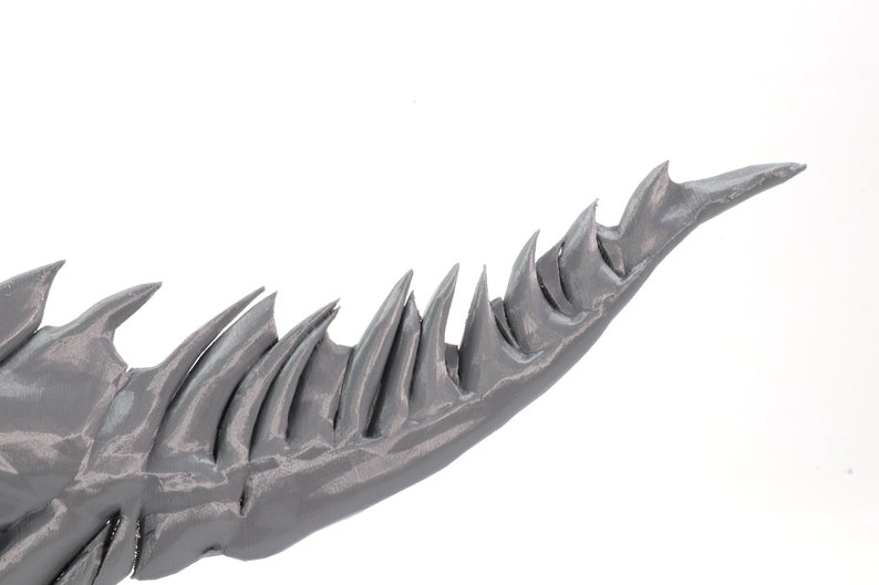 May include: A close-up of a gray, 3D printed, spiky tail with a sharp point.