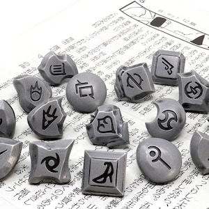 May include: A set of 15 silver-colored metal tokens with different symbols engraved on them. The tokens are scattered on a newspaper background.