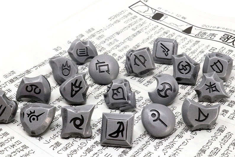 May include: A set of 15 silver-colored metal tokens with different symbols engraved on them. The tokens are scattered on a newspaper background.