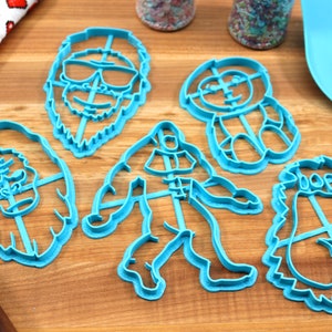 May include: Set of five blue plastic cookie cutters shaped like a yeti, a sasquatch, a yeti with sunglasses, a yeti with a hat, and a yeti with a beard.