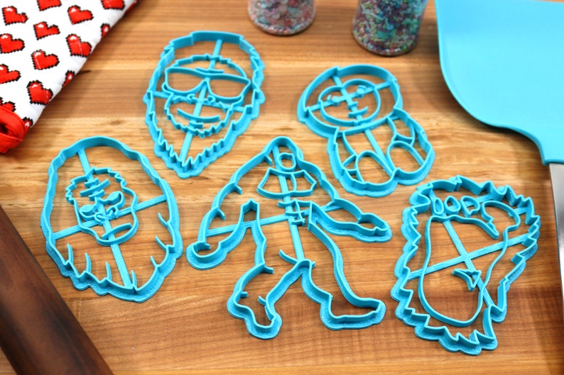 May include: Set of five blue plastic cookie cutters shaped like a yeti, a sasquatch, a yeti with sunglasses, a yeti with a hat, and a yeti with a beard.