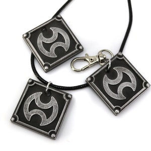 May include: Three silver-colored pendants with a black background and a stylized symbol. The pendants are attached to a black cord necklace.