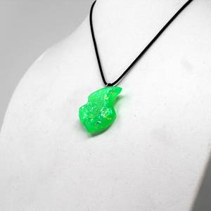 Op de afbeelding: Een ketting met een groene opaal hanger aan een zwart koord. De opaal heeft een vrije vorm, is lichtgroen en heeft een iriserende glans.