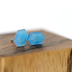 K&ouml;nnte beinhalten: Ein Paar blaue geometrische Ohrstecker. Die Ohrringe sind aus einem durchsichtigen Material gefertigt und haben eine leicht irisierende Oberfl&auml;che.