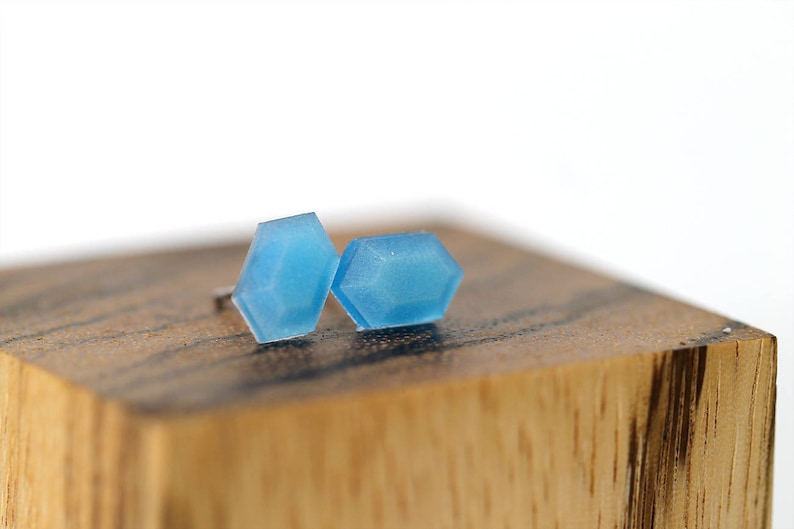 K&ouml;nnte beinhalten: Ein Paar blaue geometrische Ohrstecker. Die Ohrringe sind aus einem durchsichtigen Material gefertigt und haben eine leicht irisierende Oberfl&auml;che.