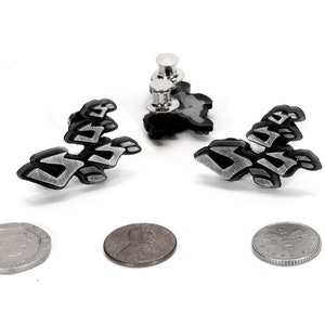 May include: Two silver and black enamel pins with a stylized design. The pins are attached to a white background.