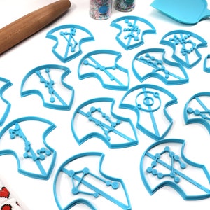 Puede incluir: Un juego de 13 cortadores de galletas de pl&aacute;stico azul con forma de constelaciones. Los cortadores est&aacute;n dispuestos sobre una superficie blanca.